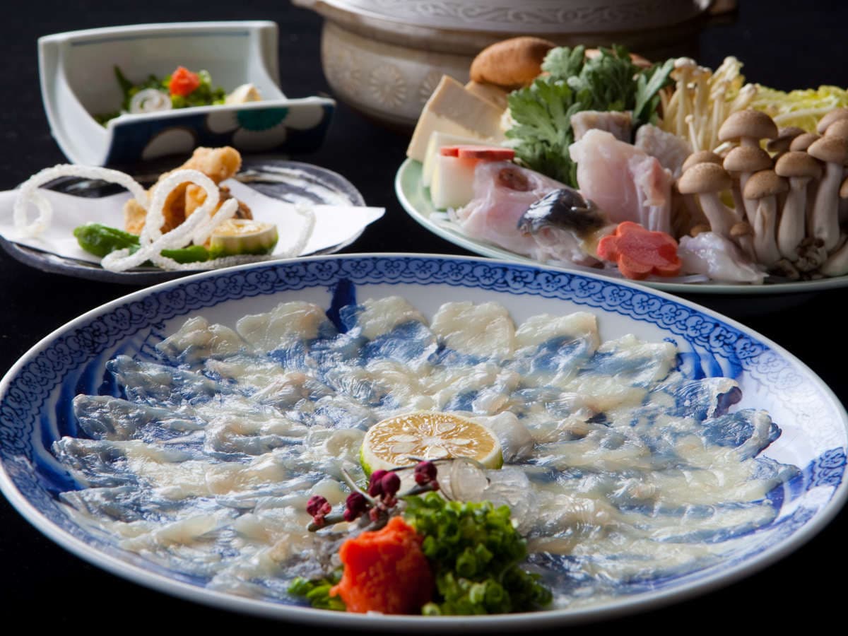 Fugu pufferfish course with thin sashimi fanned on a blue plate beside hotpot vegetables and mushrooms, Ryokan Sennari, Beppu Onsen
