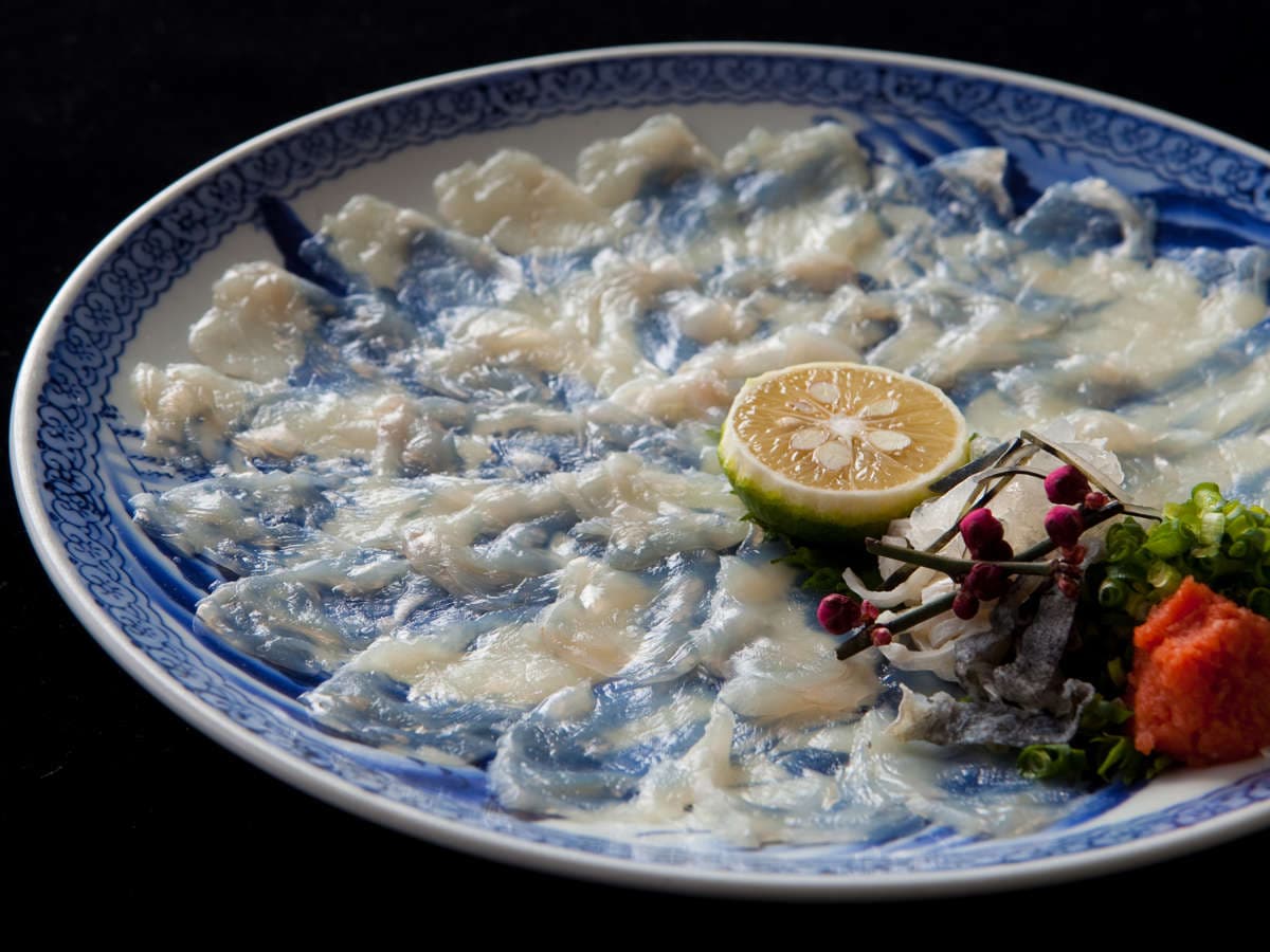 Close-up of fugu sashi, translucent pufferfish slices fanned on a blue-and-white plate with sudachi, Ryokan Sennari, Beppu Onsen