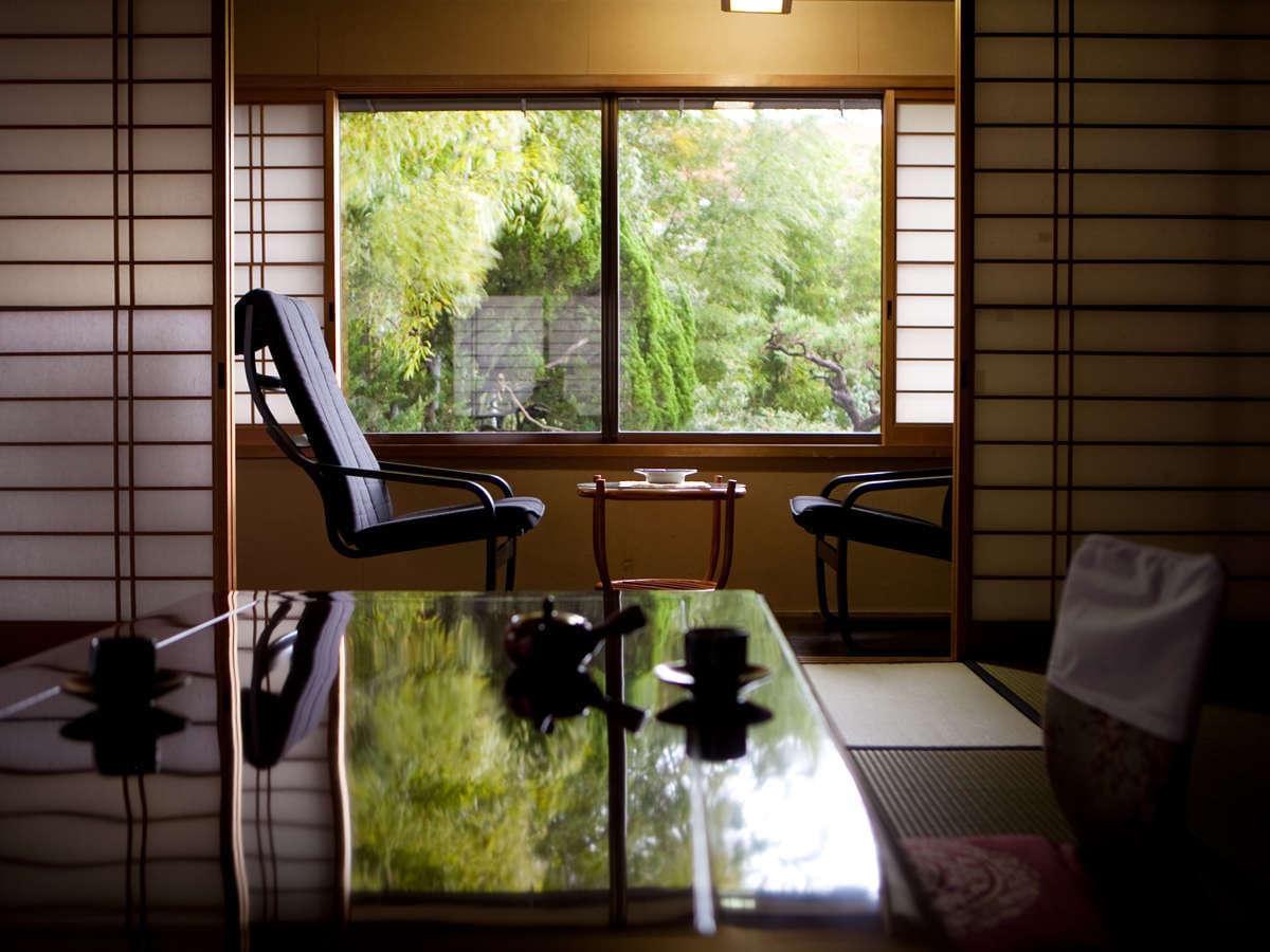 Tatami guest room with lacquered low table and armchairs by a shoji window overlooking a green garden, Ryokan Sennari, Beppu Onsen