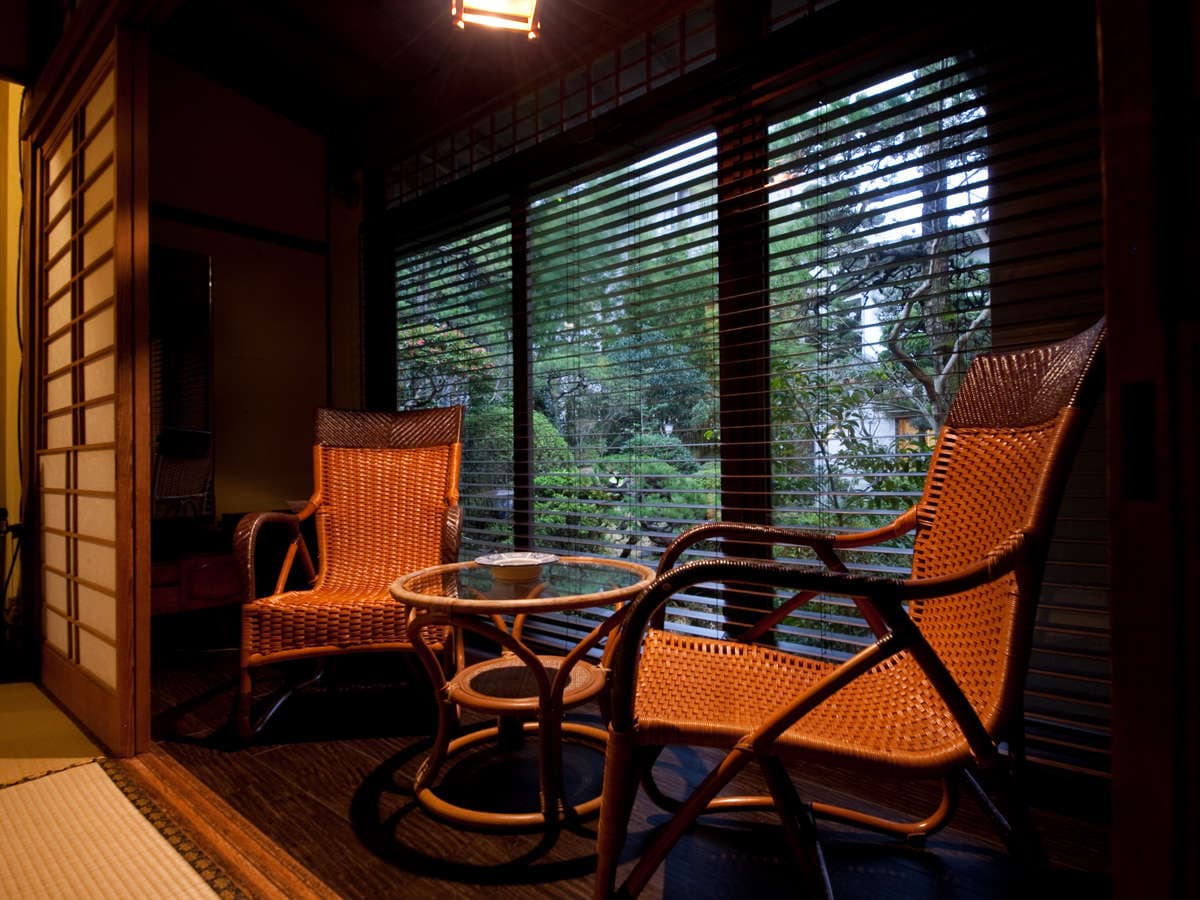 Cozy hiroen sitting alcove with woven rattan chairs and a glass table facing a garden view, Ryokan Sennari, Beppu Onsen