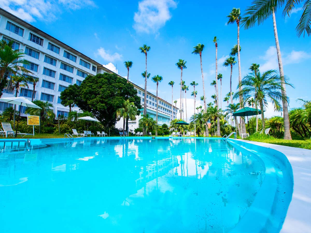 Outdoor swimming pool at Ibusuki Phoenix Hotel framed by tall palm trees and the resort building