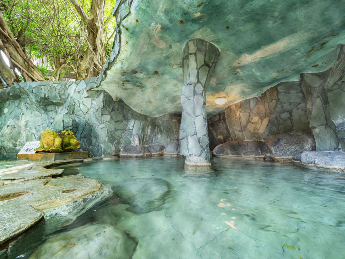 Cave-style indoor hot spring bath at Ibusuki Phoenix Hotel with carved stone pillars and clear blue-green water