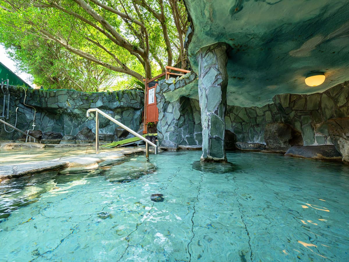Open-air rock rotenburo onsen bath at Ibusuki Phoenix Hotel set into a stone grotto surrounded by greenery