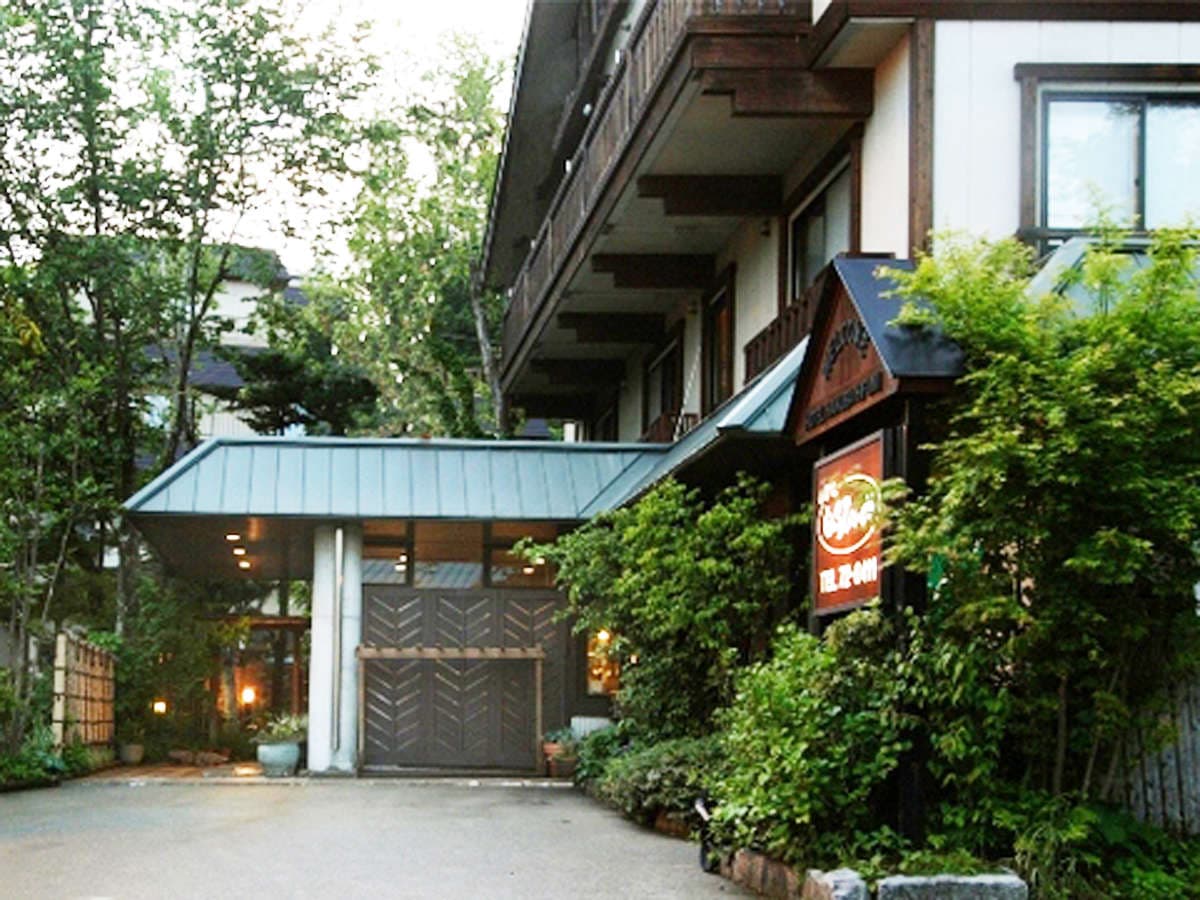 Wooden front entrance of Hakuba Hifumi nestled among trees in Hakuba Happo Onsen at dusk