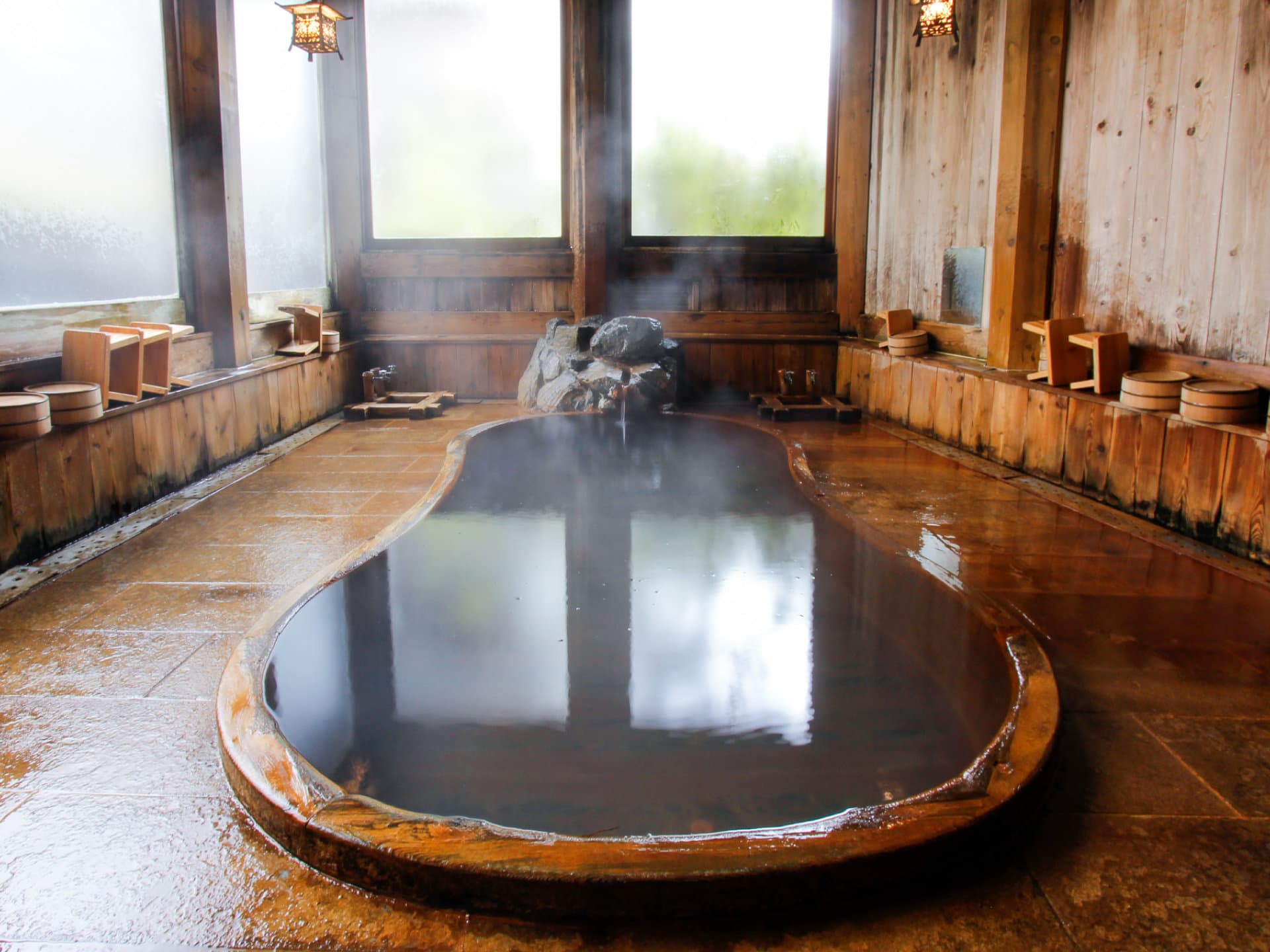Kamakura-buro indoor bath, a large stone-rimmed pool with steam rising to tall windows