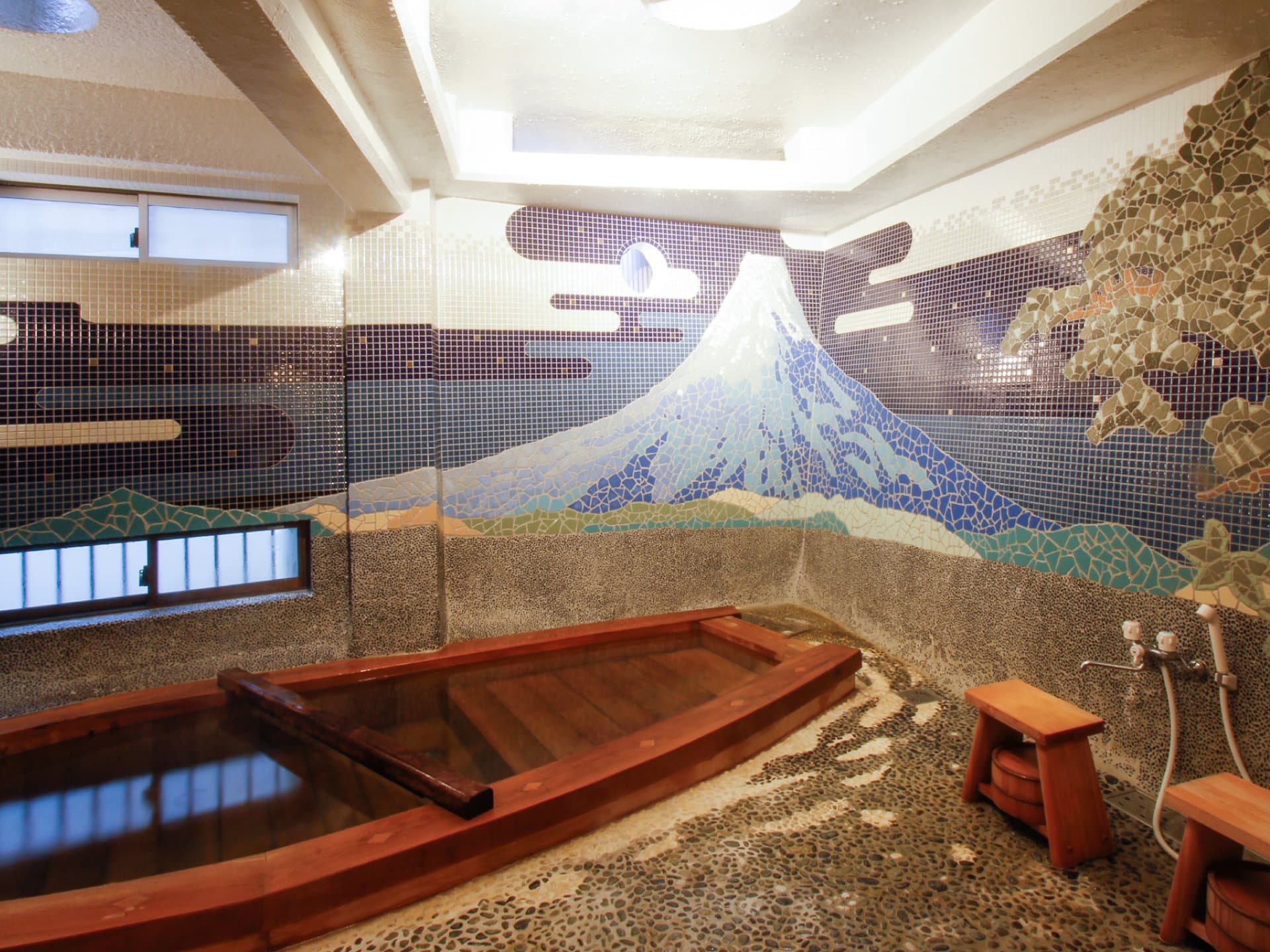 Private bath with a boat-shaped wooden tub facing a tiled Mount Fuji mosaic