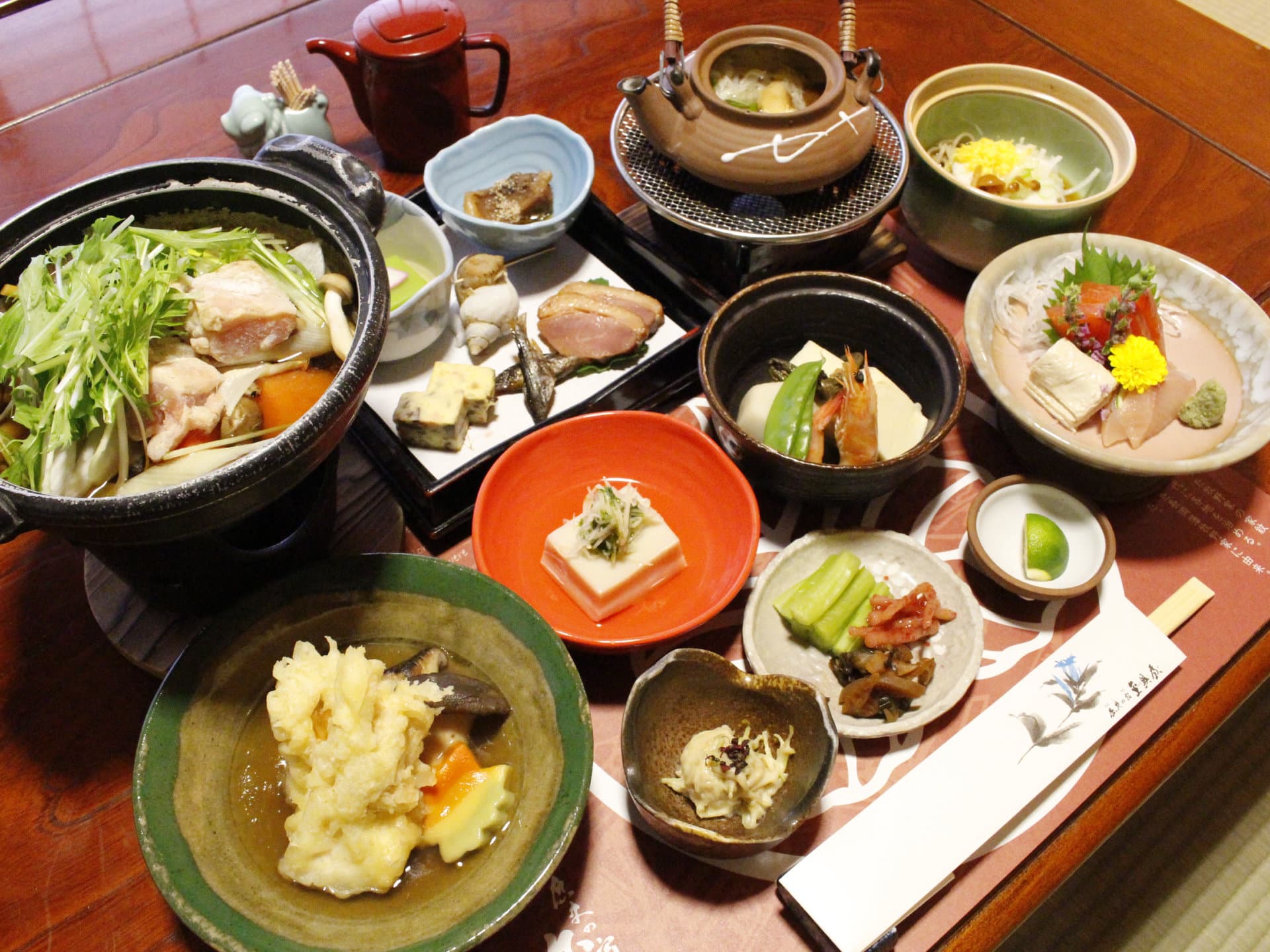 Multi-course kaiseki dinner on a lacquer tray with a clay hotpot and sashimi