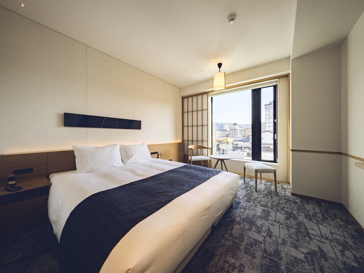 Comfort double guest room with crisp white bedding and a window framing the Takayama townscape and mountains