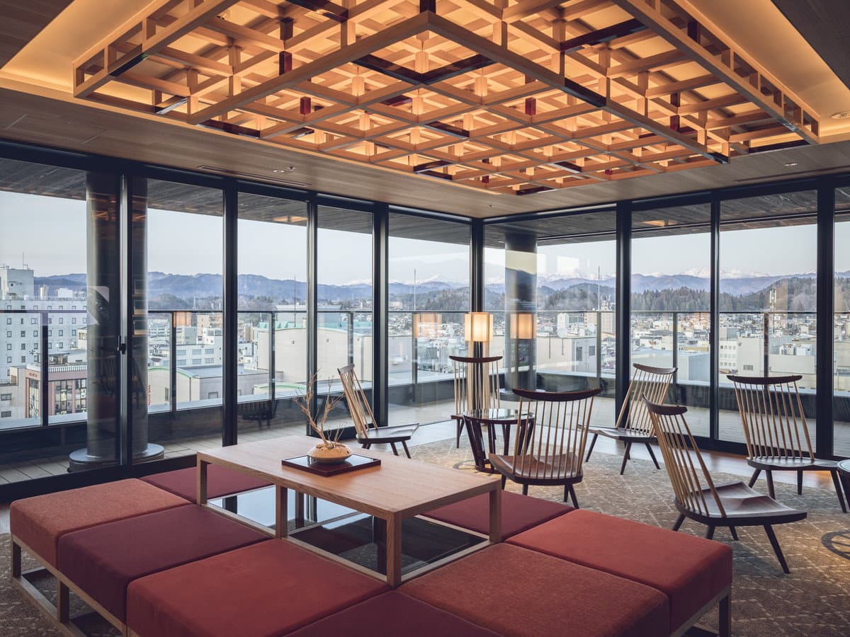 Top-floor lounge with a lattice ceiling and panoramic windows over Takayama town and the surrounding mountains