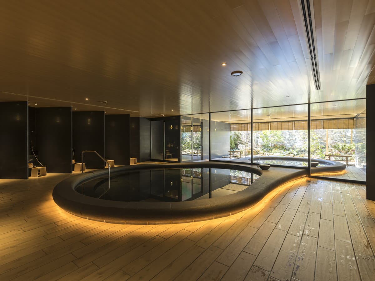 Sculptural curved indoor onsen pool with warm rim lighting and a view onto the garden at Tokyu Stay Hida Takayama