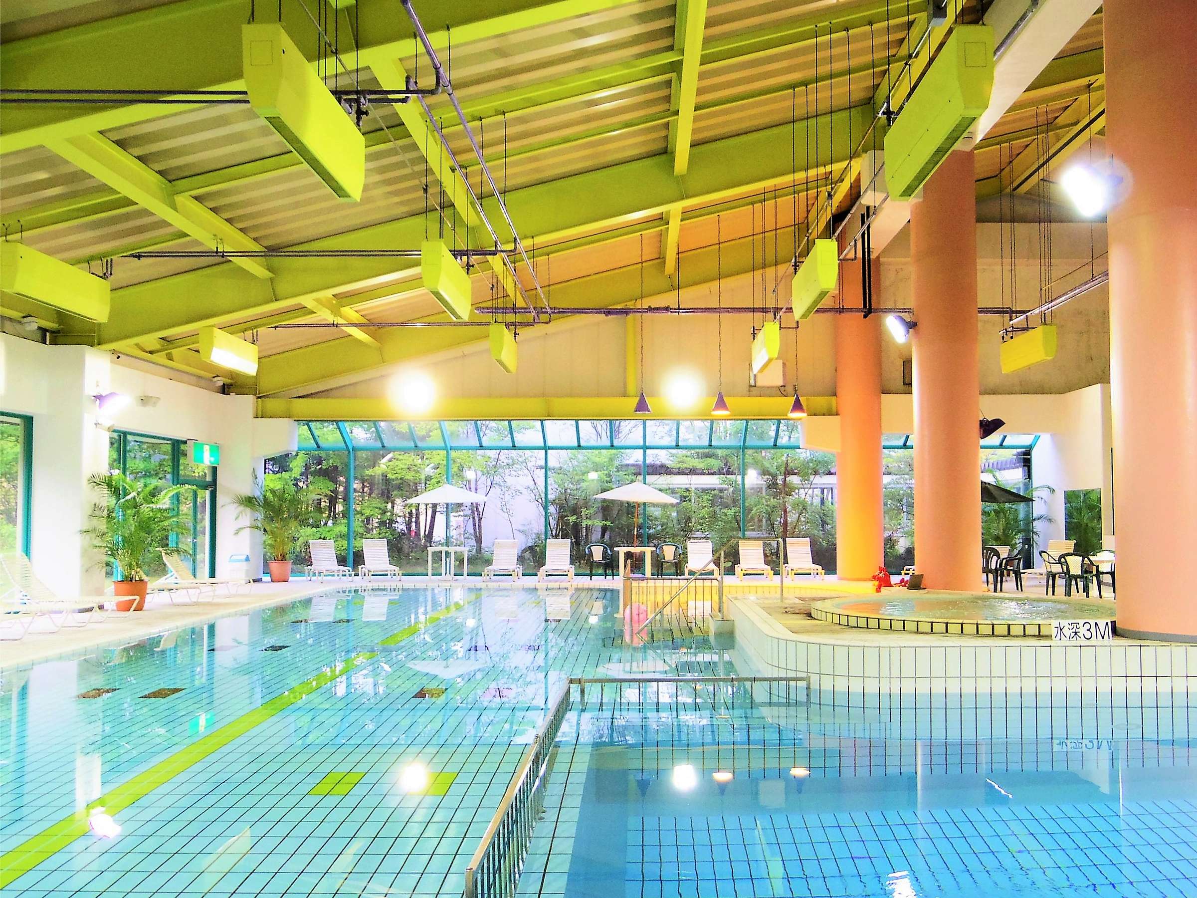 Kusatsu Now Resort Hotel large indoor swimming pool under a green-painted vaulted roof with garden-facing glass wall