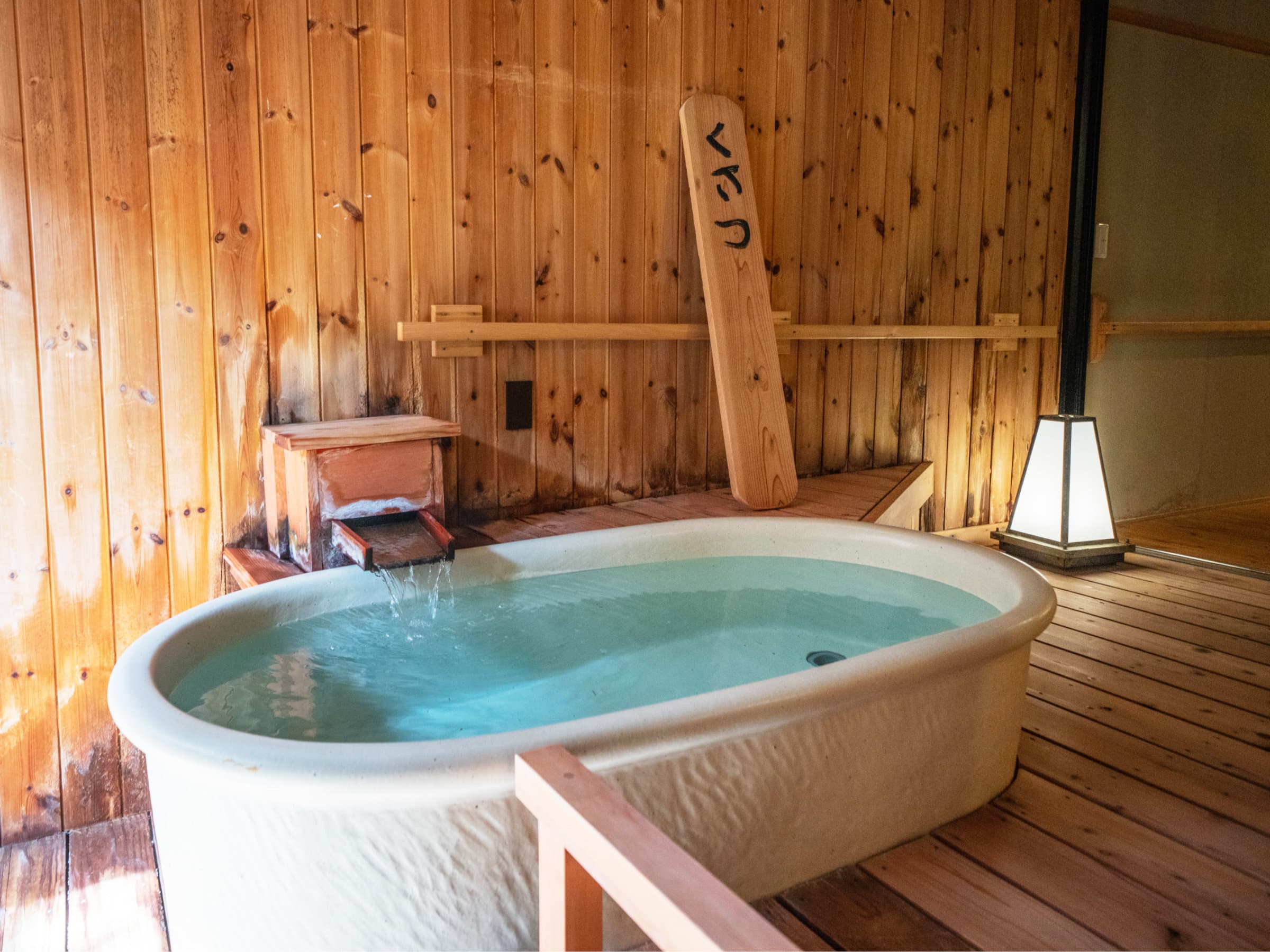 Kusatsu Now Resort Hotel private cypress-walled bath with a white oval tub and water flowing from a wooden spout