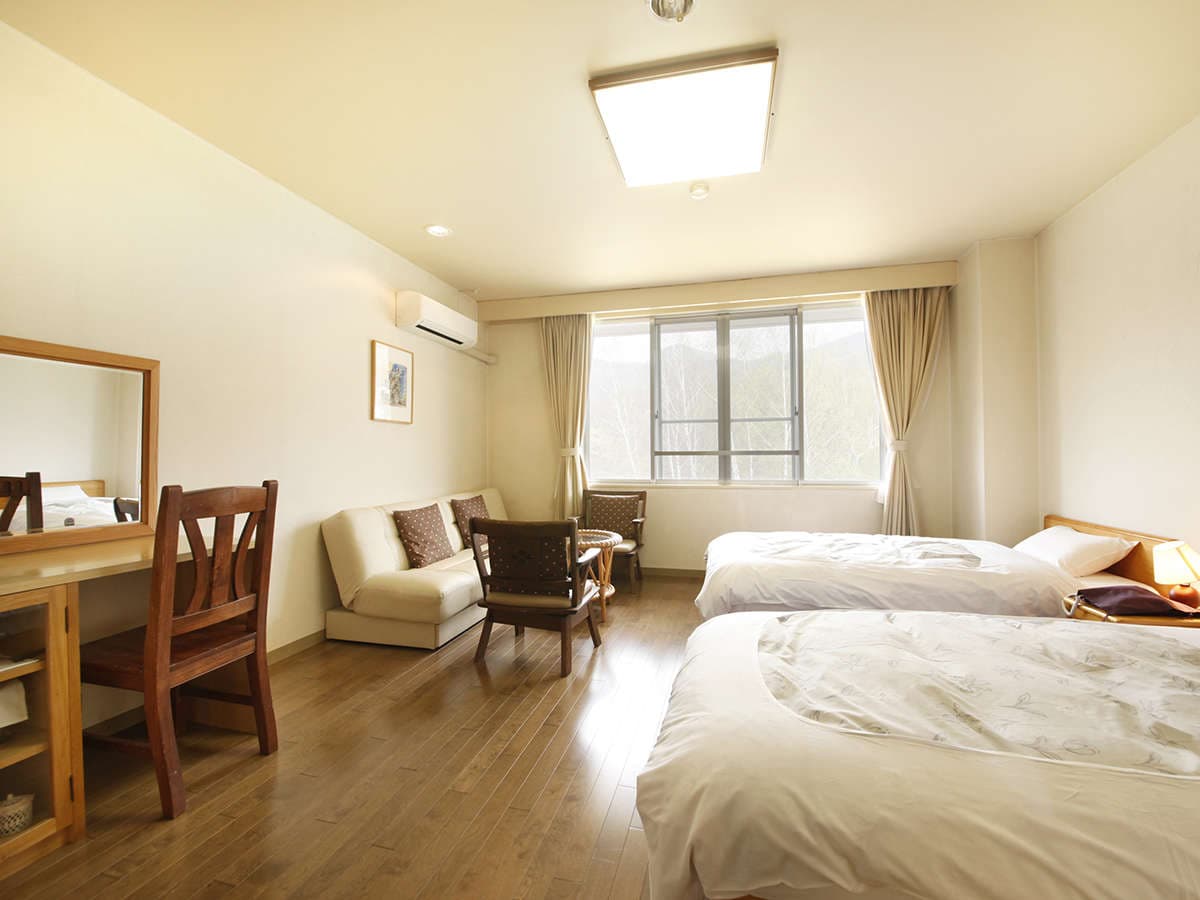 Bright Western-style twin guest room with sofa, wooden floor and a window framing the Zao forested hills