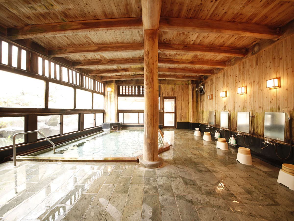 Spacious indoor stone bath with timber pillars and large windows at Hotel Matsukaneya Annex in Zao