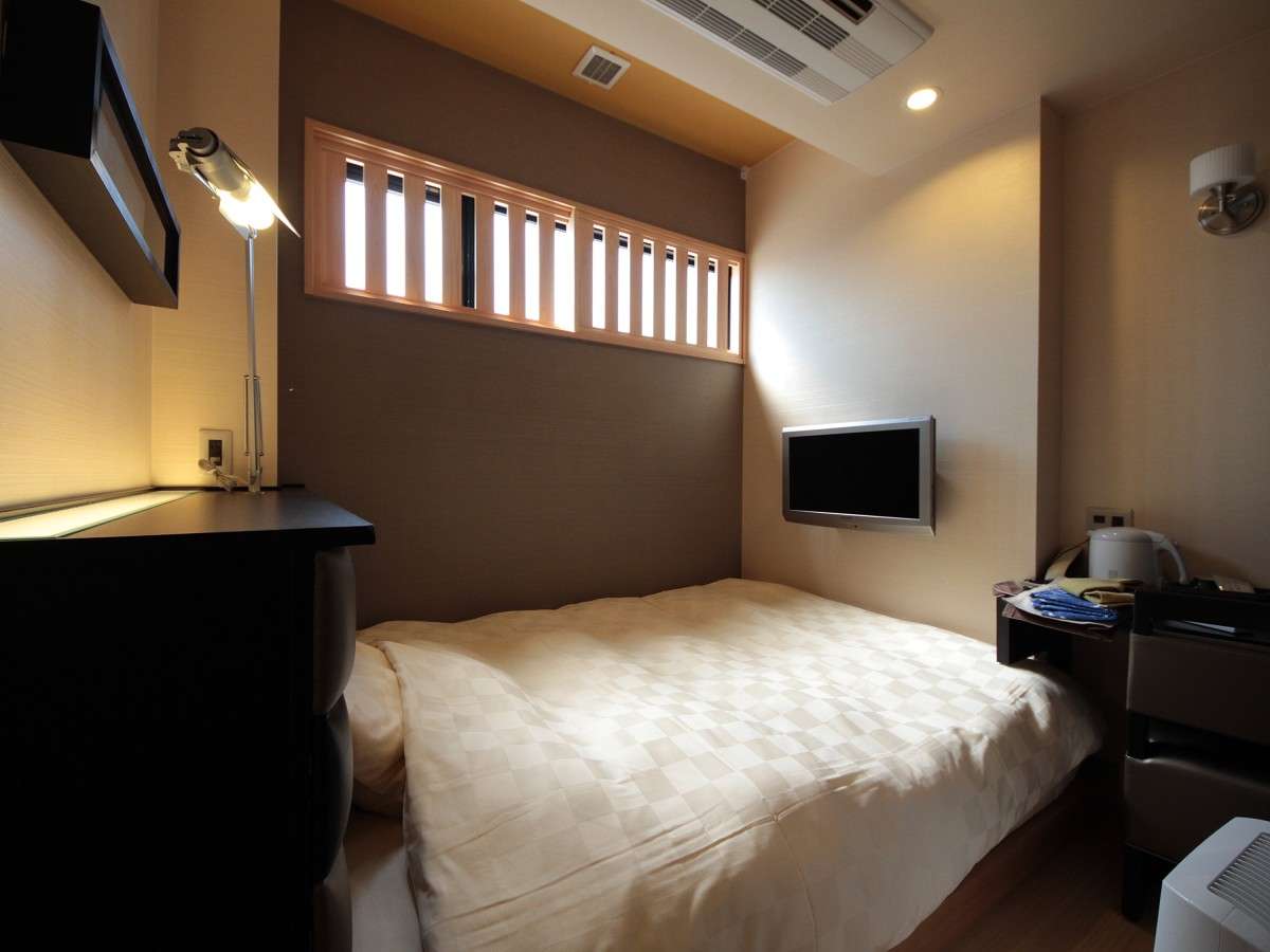 Cozy single guest room with a double bed, wall-mounted TV and a slatted clerestory window