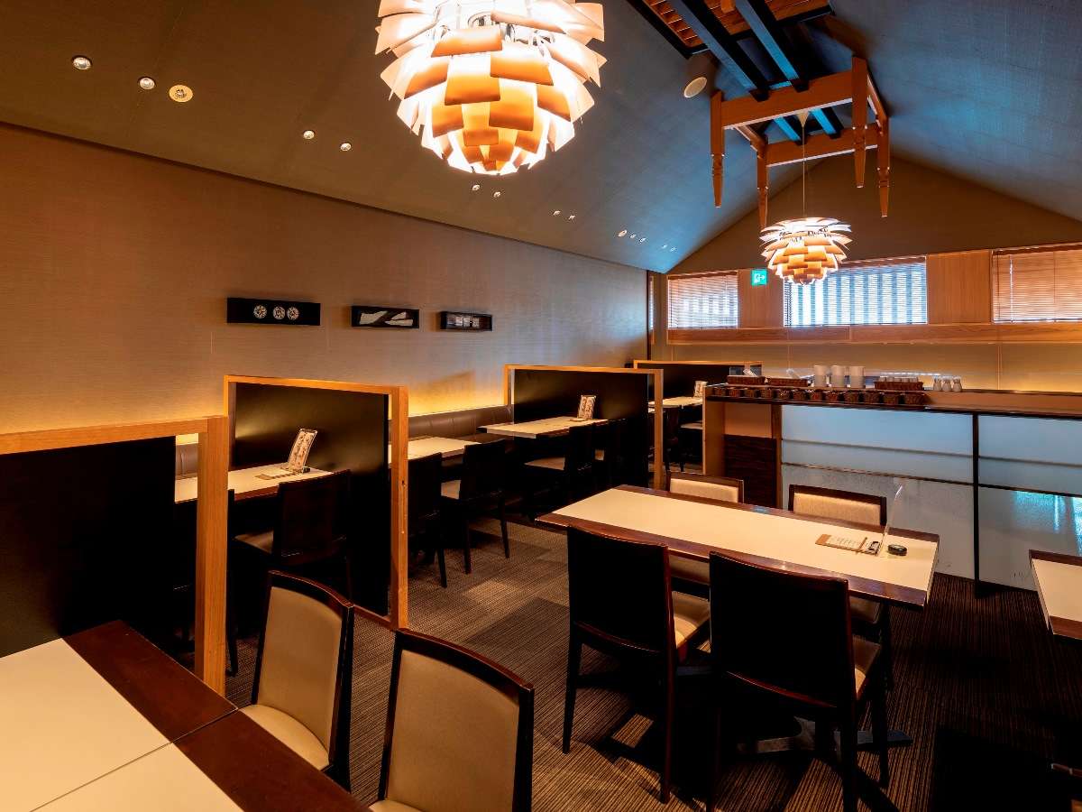 Dining hall with private semi-partitioned tables under sculptural pendant lights and a vaulted ceiling