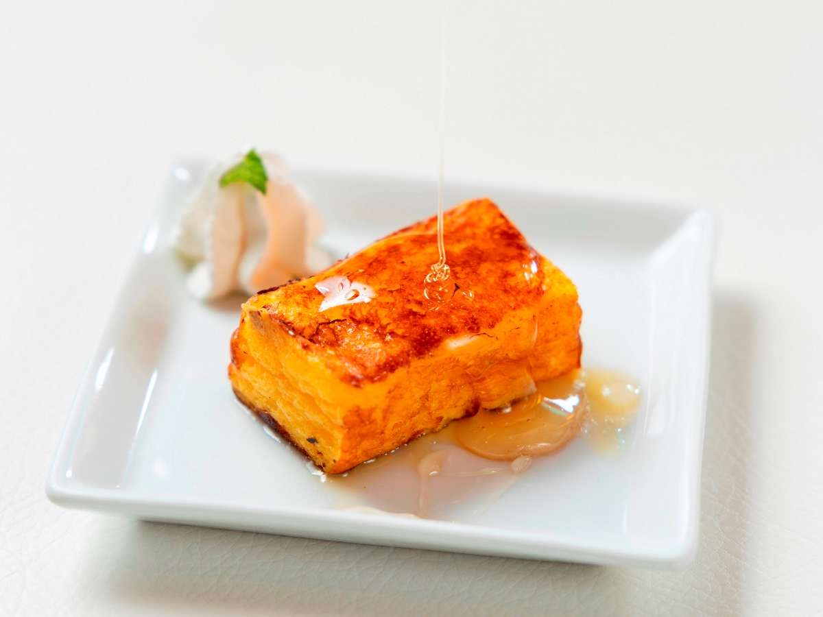 Plated French toast drizzled with honey and topped with whipped cream and mint, served at breakfast