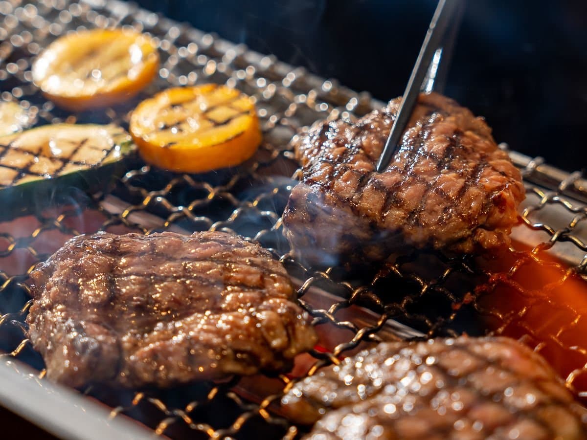 Joshu wagyu and pork sirloin grilling over a charcoal grate with grilled lemon and zucchini