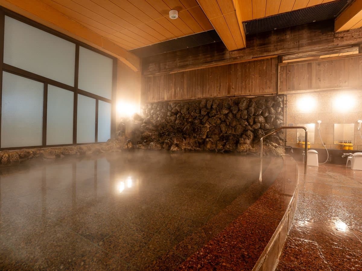 Indoor public bath fed by Sainokawara source with a rock wall and steam over the stone-rimmed pool