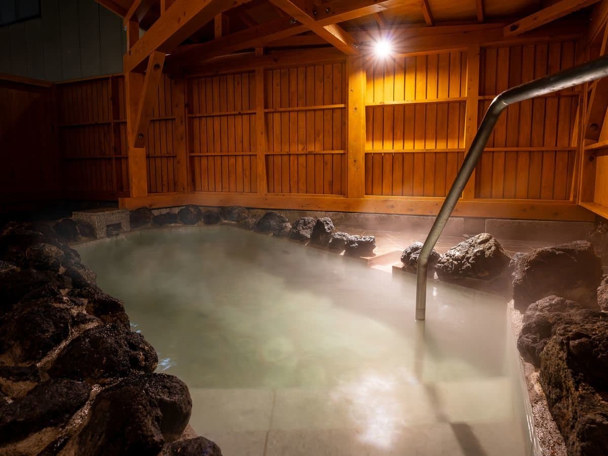 Outdoor rotenburo bath fed by the Yubatake source surrounded by lava rock under a wooden roof