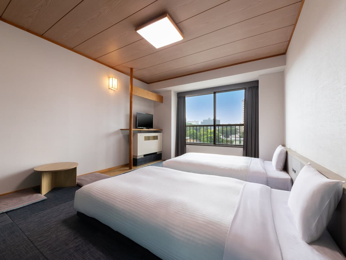 Deluxe Japanese-style twin room with low beds, wood ceiling and a window framing green hillside