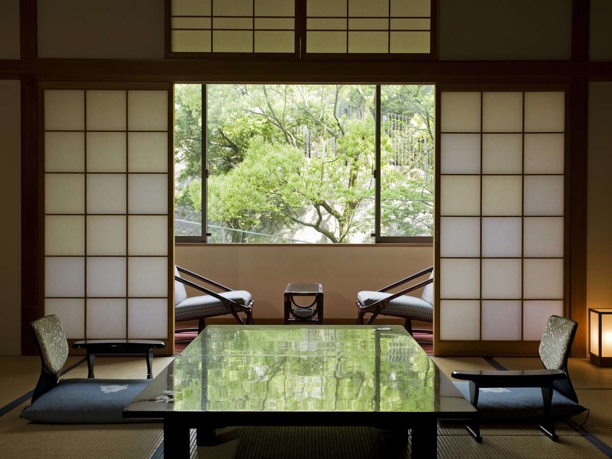 Tatami guest room at Hotel Tsubakikan looking out through wide windows onto green garden foliage