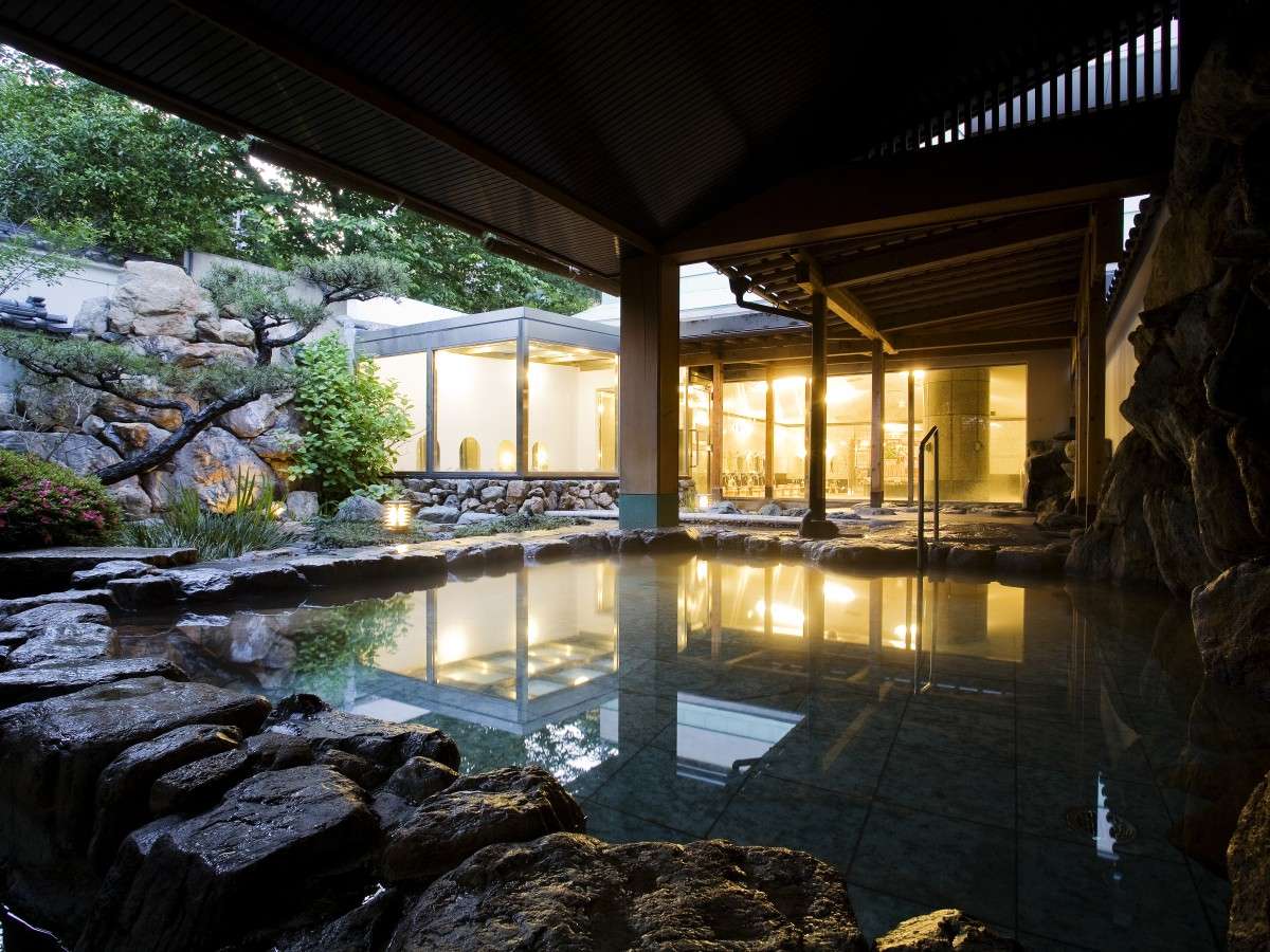 Open-air rotenburo hot-spring bath at Hotel Tsubakikan at dusk with rock garden and lantern glow