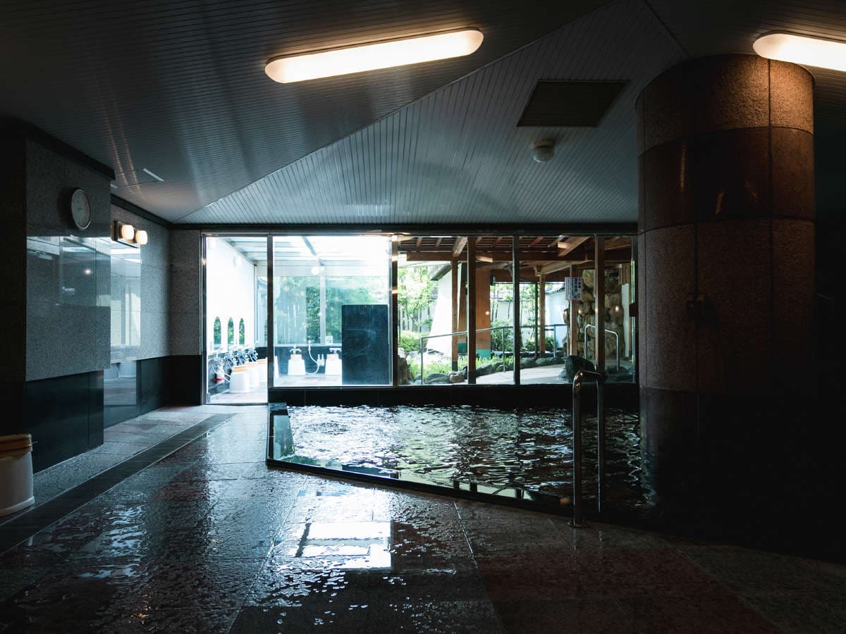 Spacious indoor hot-spring bath at Hotel Tsubakikan with stone walls opening to a garden view