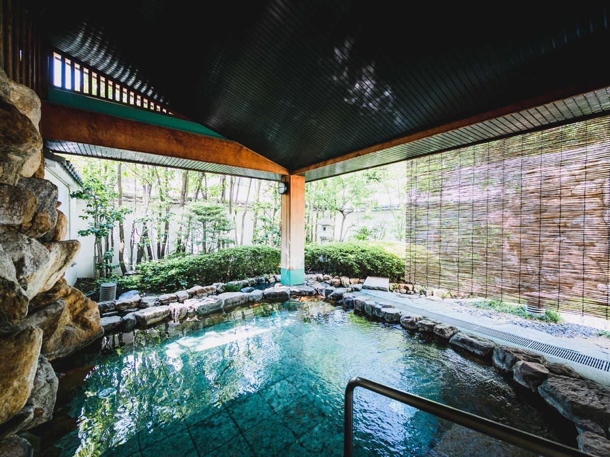 Outdoor stone-rimmed onsen bath at Hotel Tsubakikan framed by bamboo screens and greenery