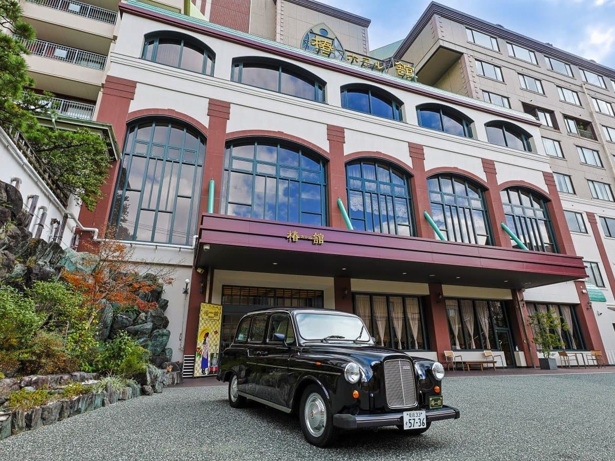 Hotel Tsubakikan facade in Dogo Onsen with a classic black taxi parked at the arched entrance