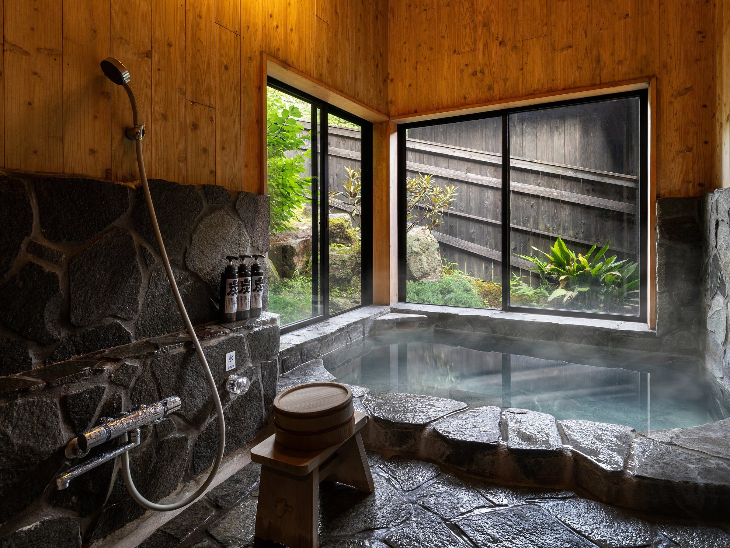 Private open-air stone rotenburo bath at Yufuin Yufusaryo overlooking lush green foliage