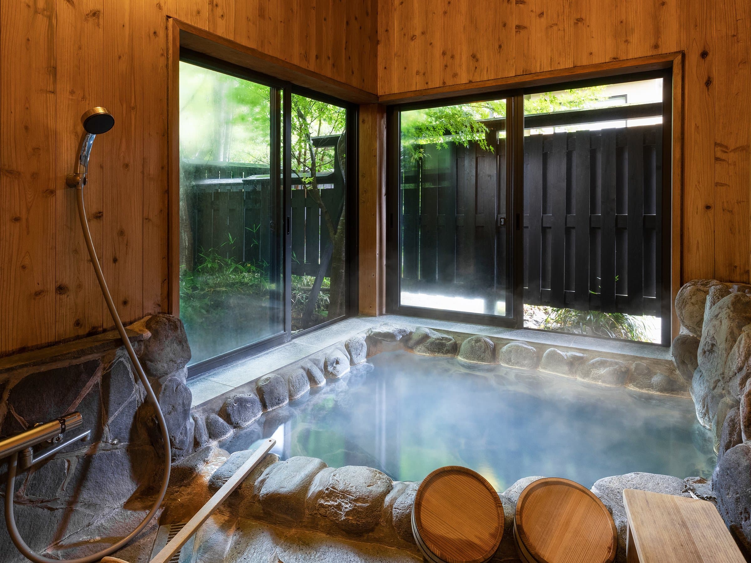 Outdoor stone soaking bath with wooden tubs and a garden view at Yufuin Yufusaryo