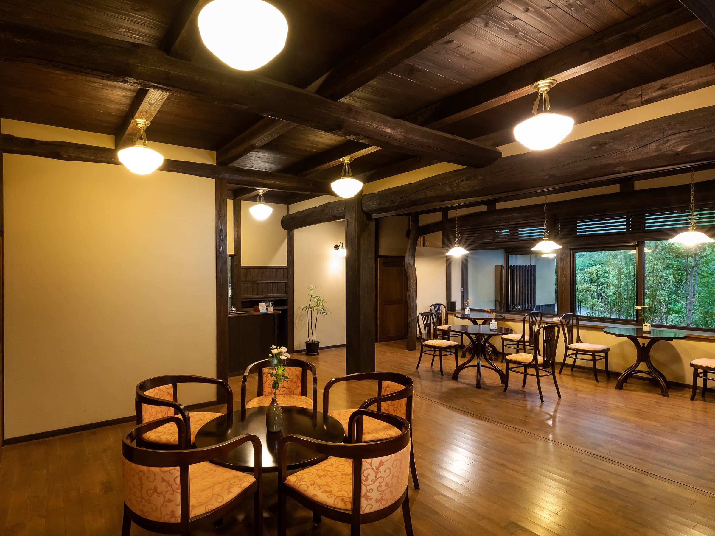 Warm wooden lounge with cafe seating and a beamed ceiling at Yufuin Yufusaryo