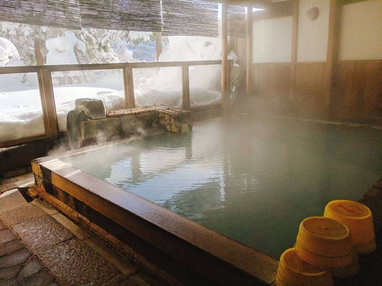 Steaming outdoor onsen bath surrounded by deep snow and a stone lantern at Zao Plaza Hotel