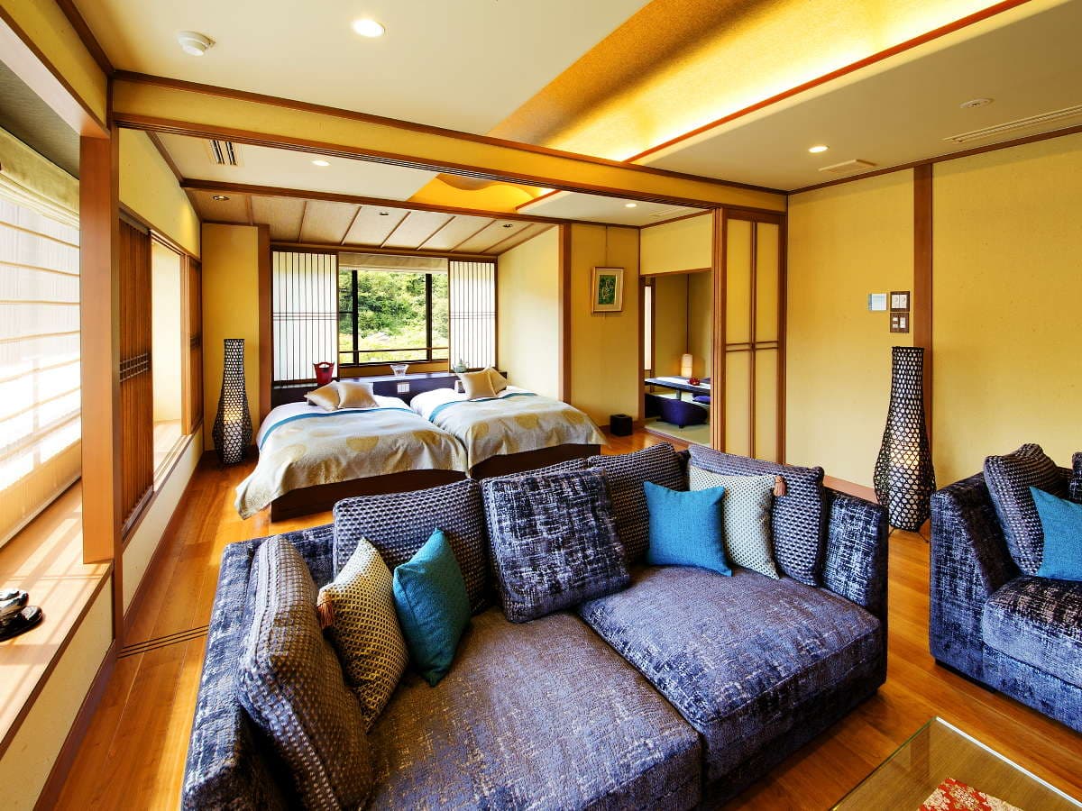 Modern Japanese guest room with twin low beds, sofa and large garden-view window at Kanazawa Yuwaku Onsen Hyakurakuso