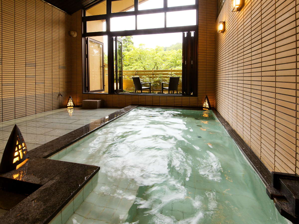 Indoor hot-spring bath with tiled walls and a window opening to greenery at Hyakurakuso, Yuwaku Onsen