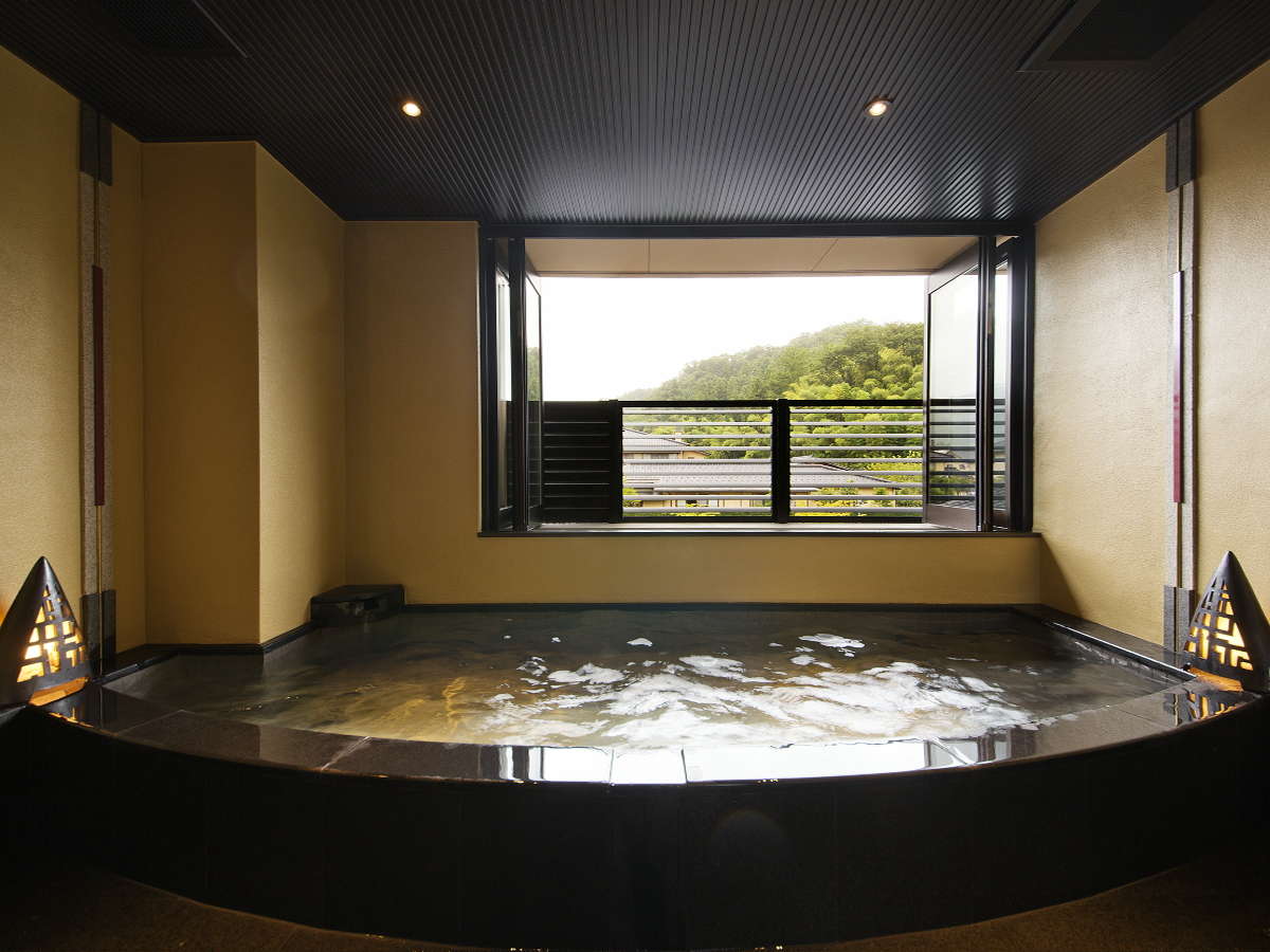 In-room private hot-spring bath with a balcony and hillside view at Kanazawa Yuwaku Onsen Hyakurakuso