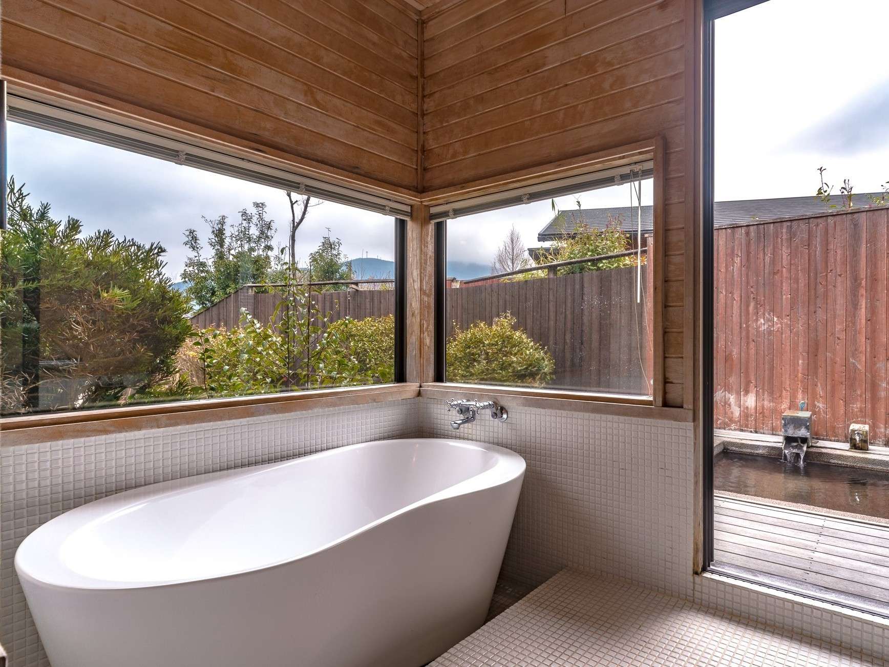 In-room freestanding soaking tub framed by corner windows looking onto the garden
