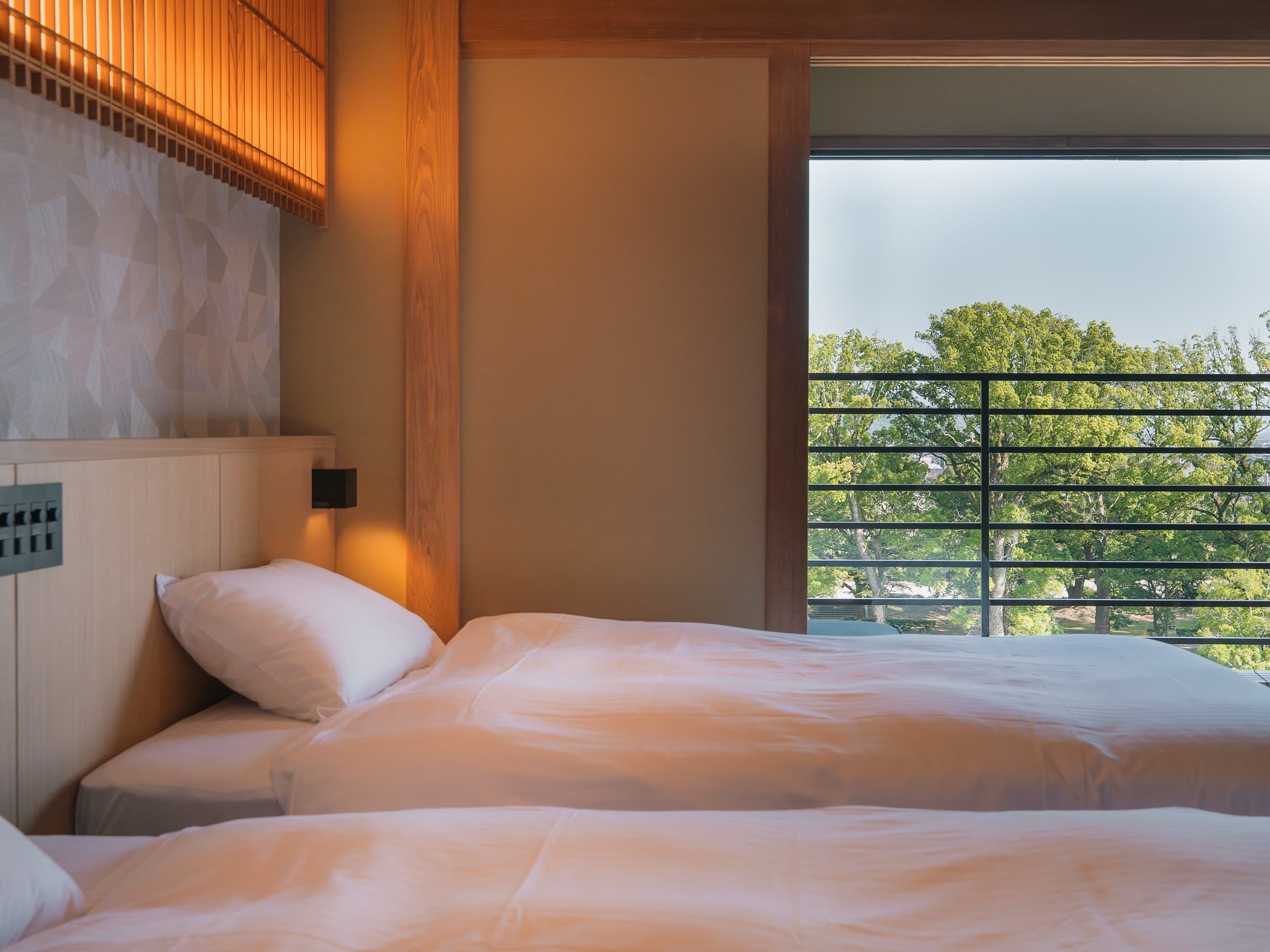 Twin-bed guest room blending tatami and modern decor with a balcony overlooking trees at Hotel Higuchiken