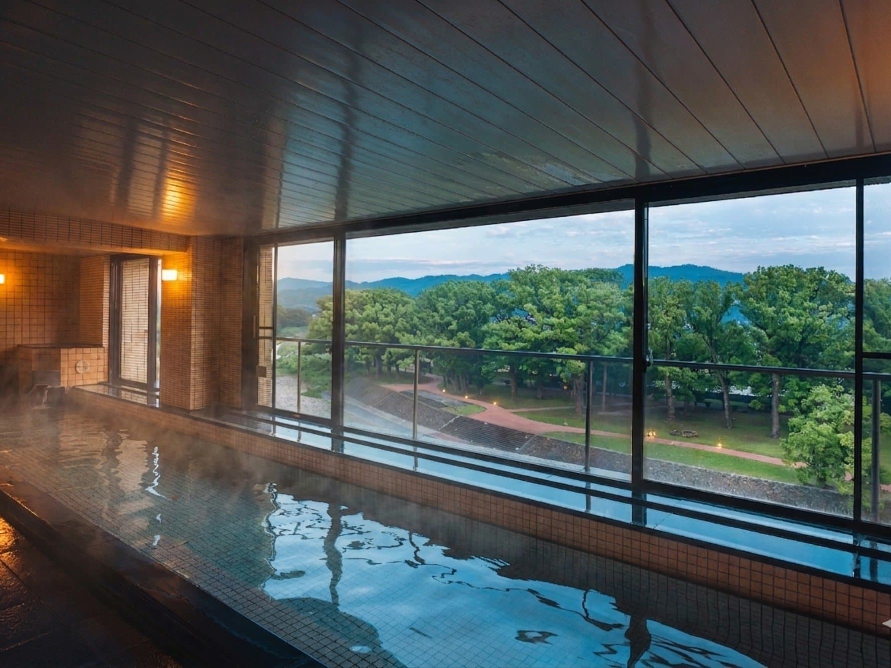 Indoor onsen bath with steam rising and panoramic mountain view through wide windows at Hotel Higuchiken