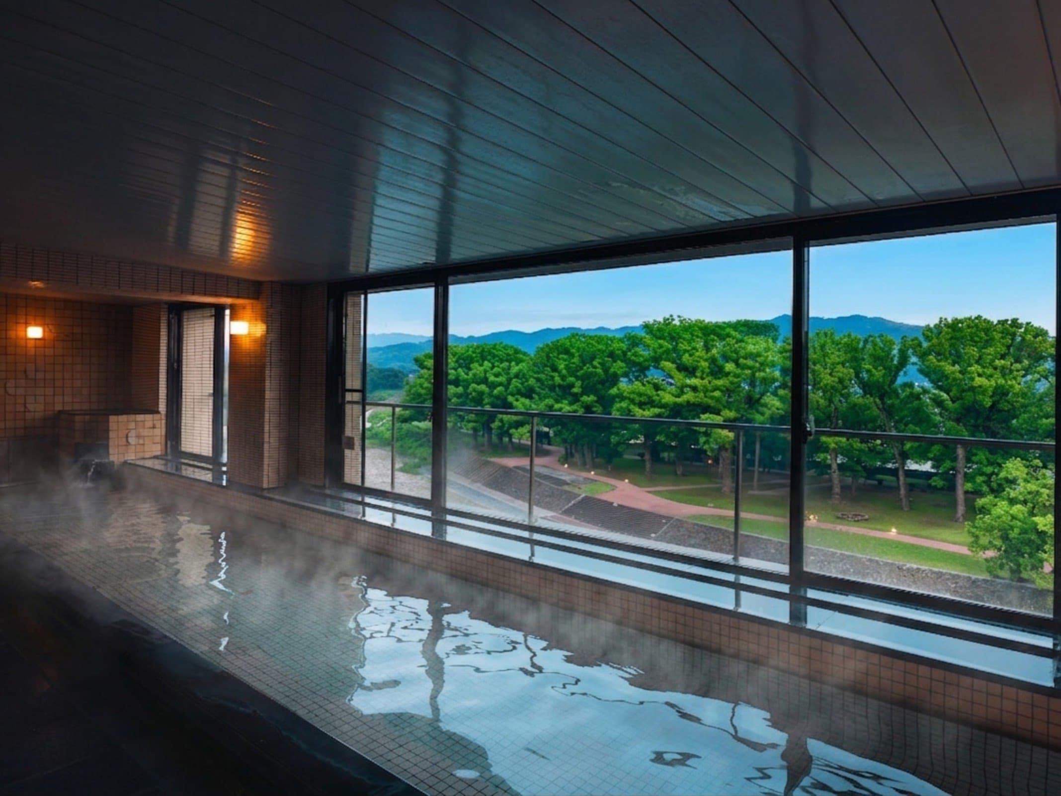 Steaming indoor hot-spring bath overlooking greenery and distant hills at Hotel Higuchiken