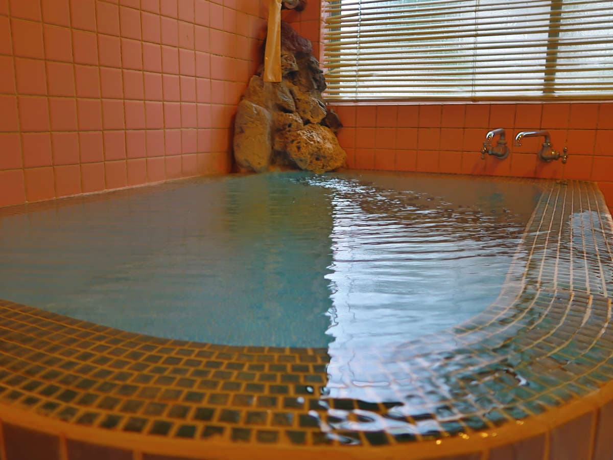 Close view of the tiled onsen bath at Ryokan Furuya with a rock water spout and clear hot spring water