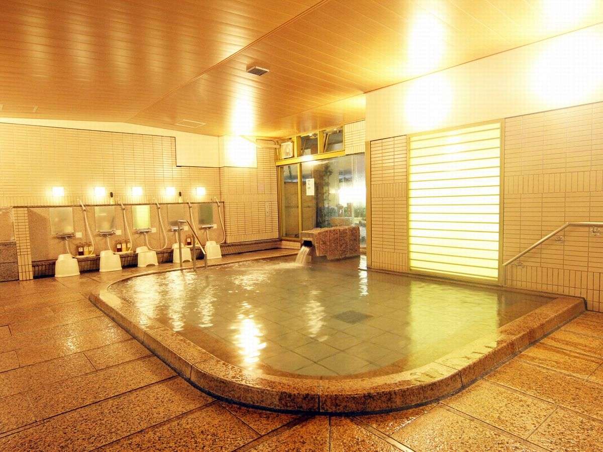 Large tiled indoor public bath with stone surround and washing stations at Miyajima Hotel Makoto