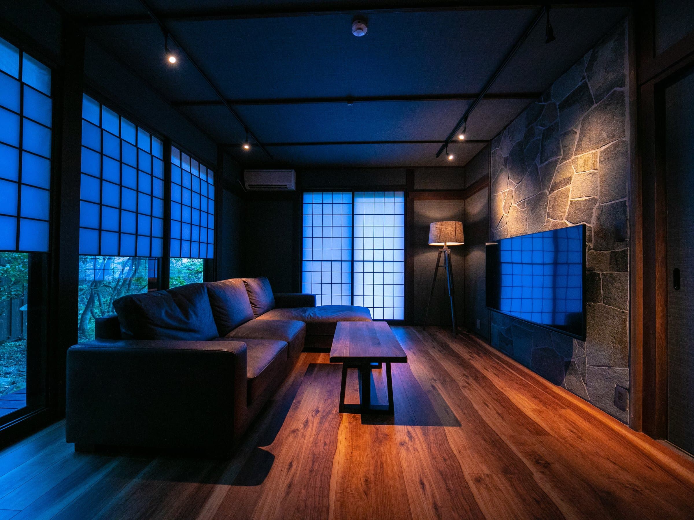 Tatami guest room with shoji screens, dark stone wall and wood floor lit at dusk at Yufuin Kazenomori