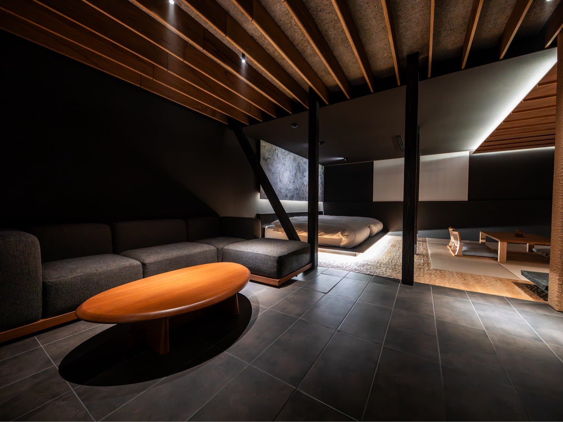 Modern designer suite with lounge seating and a low platform bed beyond timber screens at Yufuin Kazenomori