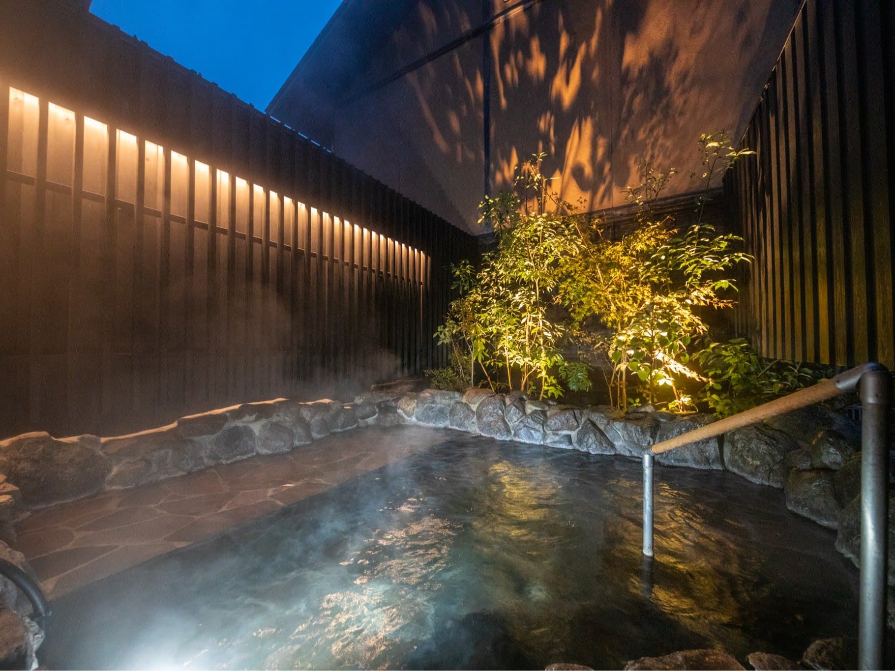 Outdoor rotenburo hot spring with rising steam and lit greenery at night at Yufuin Bettei Kazenomori