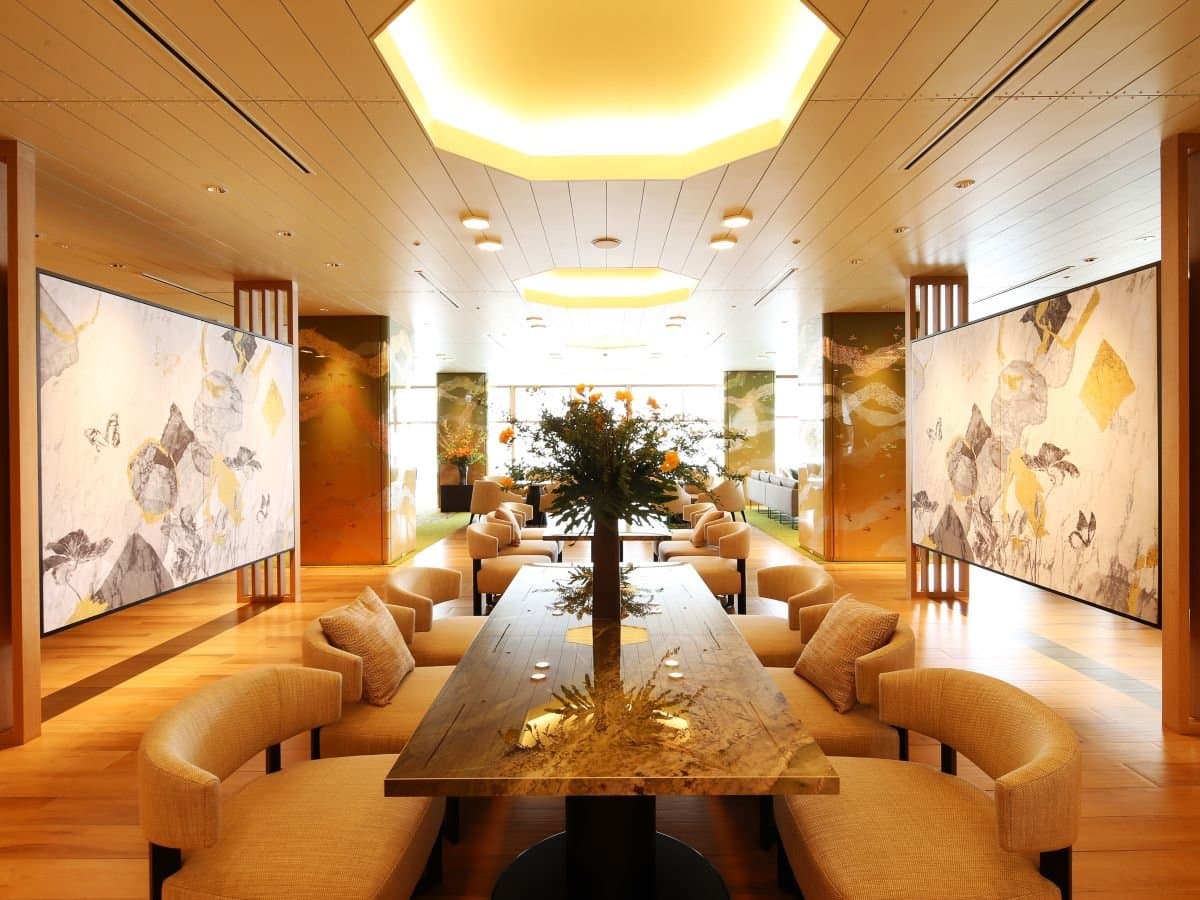 Wood-lined lounge seating area at Hotel Sakurai with a long communal table and a central ikebana arrangement
