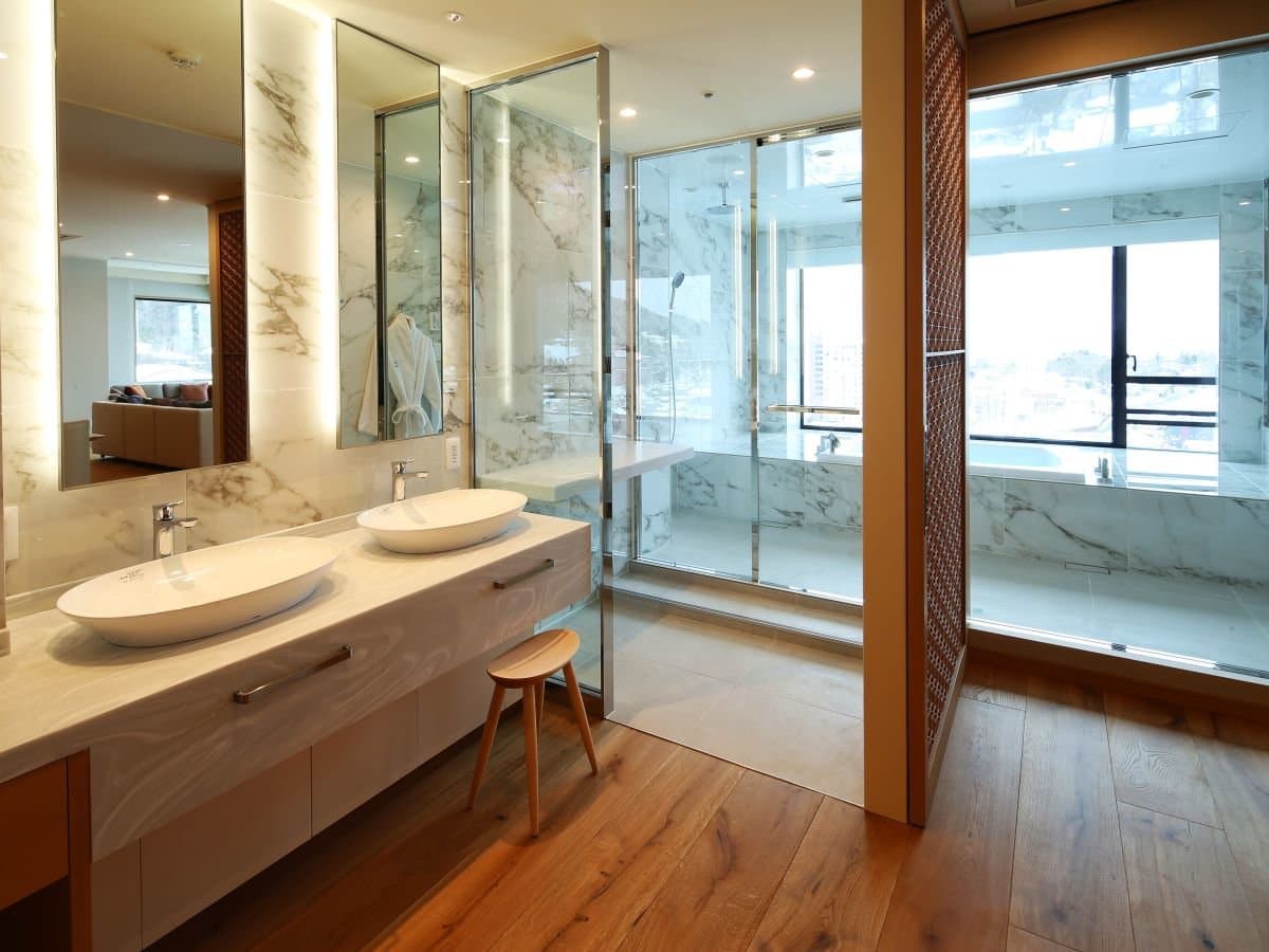 Marble bathroom of a premium suite at Hotel Sakurai with twin basins, a glass shower and a deep tub by the window
