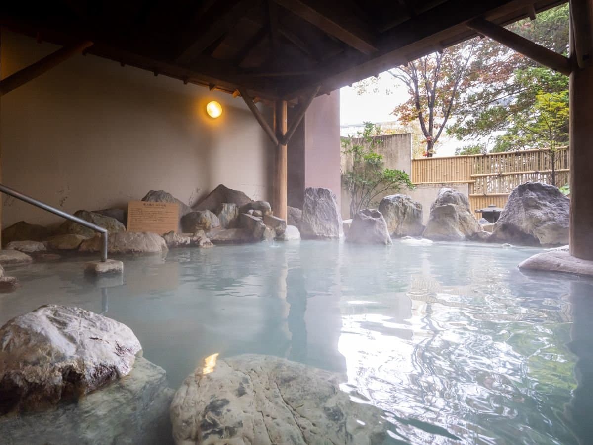 Open-air rotenburo at Hotel Sakurai with rising steam, large rocks and a timber-roofed bathing area