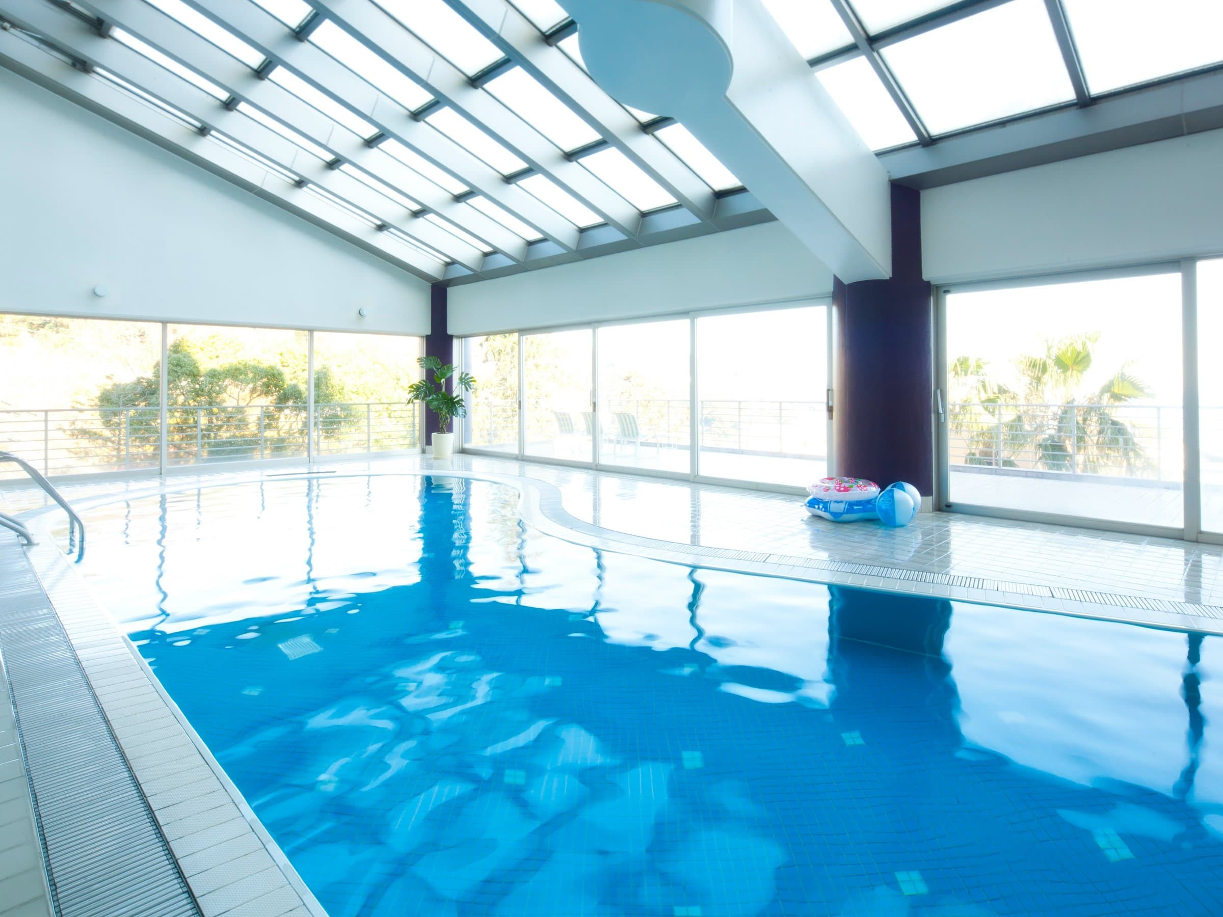 Bright glass-roofed indoor swimming pool surrounded by greenery at Risonare Atami
